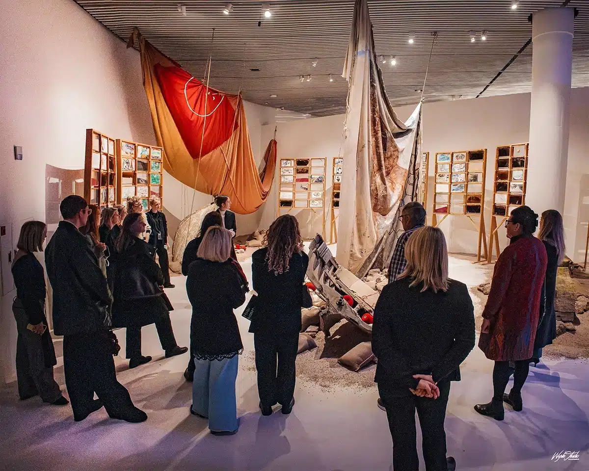Gæster står omkring skibsvrag og store sejl i rummet The Salt Traders af Anna Boghiguian på ARoS