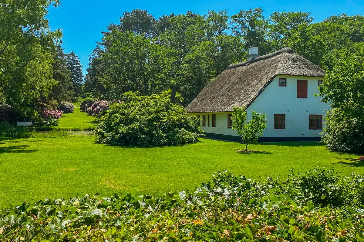 Det hvide Donbækhus med stråtag omgivet af grøn natur i Mindeparken