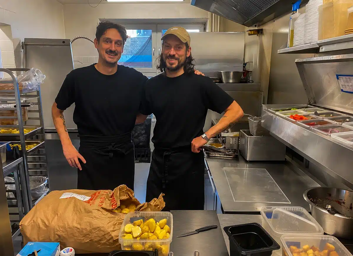 Brødrene Daniel og Marcus i sorte forklæder i Plant Foods køkken i Aarhus med en sæk kartofler og en bakke halverede kartofler foran sig
